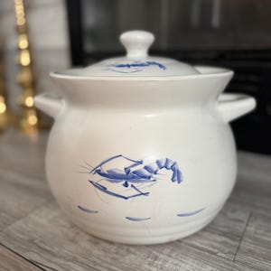 Pode incluir: Travessa de cerâmica branca com tampa e duas pegas. A travessa apresenta um desenho de camarão azul na lateral e detalhes azuis na tampa. Um item clássico de utensílios de cozinha.