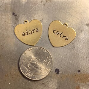 May include: Two gold heart-shaped charms with the names "adora" and "catra" engraved on them.