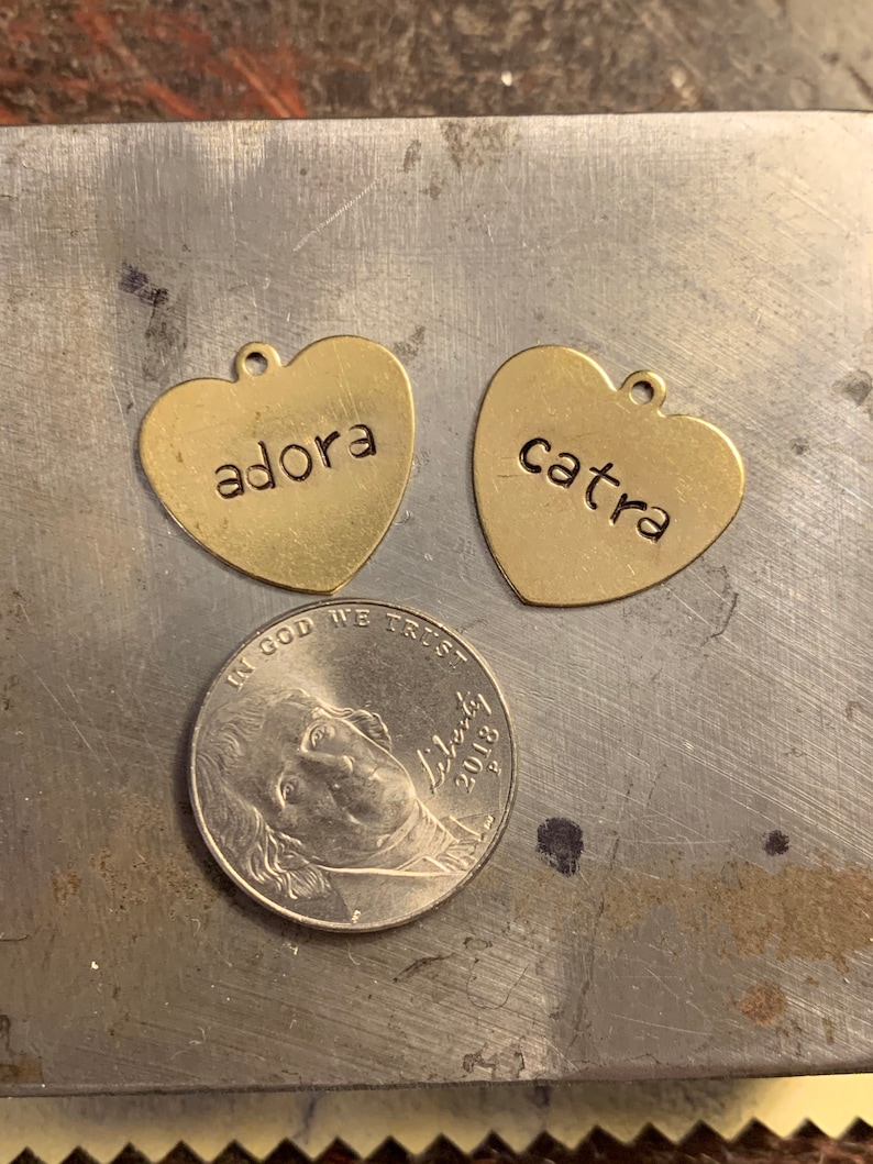 May include: Two gold heart-shaped charms with the names "adora" and "catra" engraved on them.