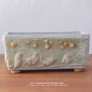 Peut inclure: Un bac à fleurs rectangulaire d'aspect vieilli avec des détails d'oiseaux et de feuillage en relief. Le bac vert clair et beige mesure 30.5 cm de long, 15.2 cm de large et 12.1 cm de haut. Le texte sur le bac indique "018-2 Medium Bird Window Box".