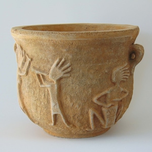 May include: A terracotta planter with a textured surface and a design of stylised figures playing musical instruments. The planter has a rounded bottom and a wide opening.