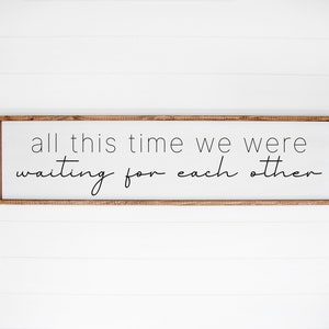 以下が含まれることがあります： 黒い筆記体で「all this time we were waiting for each other」と書かれた木製の看板です。