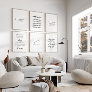 Könnte beinhalten: Eine Sammlung gerahmter, motivierender Kunstdrucke mit schwarzem Text auf weißem Hintergrund. Die Drucke zeigen Wörter wie "Erfolg", "Führung" und "Opfer". Die Kunstwerke werden in einem modernen Wohnzimmer mit weißem Sofa, Stühlen und einem Couchtisch präsentiert.
