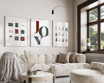 Puede incluir: Un interior de sala de estar con un sofá blanco, una mesa de café y tres impresiones enmarcadas en la pared. Las impresiones presentan diseños con temática navideña, incluyendo una impresión de arte de palabras que dice "ALEGRÍA", una impresión con un patrón de cajas de regalo y una impresión con un patrón de árboles de Navidad.