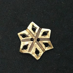 May include: A wooden button with a six-pointed star design. The star is carved with intricate lines and has a brown stain.