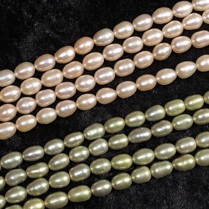 May include: Two strands of oval-shaped pearls, one strand is a light pink color and the other strand is a light green color.