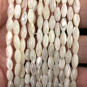 May include: A strand of white oval-shaped shell beads with iridescent accents. The beads are strung on a clear thread.