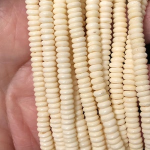 May include: A strand of off-white beads made from natural bone. The beads are small and round, with a slightly textured surface.