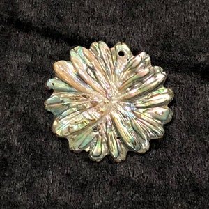 May include: A iridescent abalone shell flower pendant with a silver-toned finish. The shell has a natural, organic shape and a delicate, intricate design.