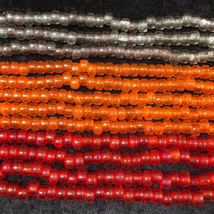 May include: A close-up of three strands of beads. The top strand is made of clear glass beads, the middle strand is made of orange glass beads, and the bottom strand is made of red glass beads.