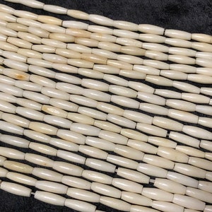 May include: A strand of off-white, smooth, cylindrical beads. The beads are all the same size and shape, and they are strung together on a clear thread.