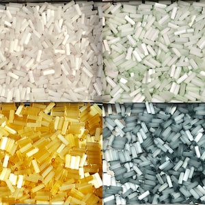 May include: Four containers of glass beads in different colors: white, light green, gold, and gray. The beads are all cylindrical in shape.