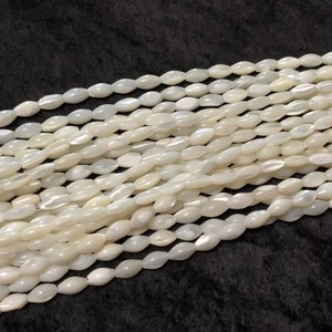 May include: A strand of white oval-shaped mother of pearl beads. The beads have a slight iridescent sheen.