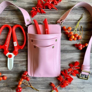 Pu&ograve; includere: Cintura da giardinaggio in pelle rosa con due tasche e una cinghia. La cintura ha due forbici da giardino rosse e un paio di forbici da potare rosse con manico bianco. Le forbici sono etichettate "Hand Creation" e "Han"