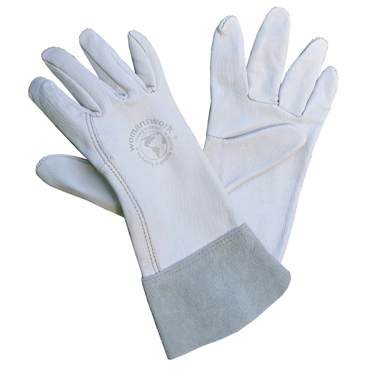May include: A pair of white leather gloves with a grey cuff. The gloves are designed for work and have a stitched seam detail. The left glove has a logo that reads "womanswork - happy women building a gentle world".