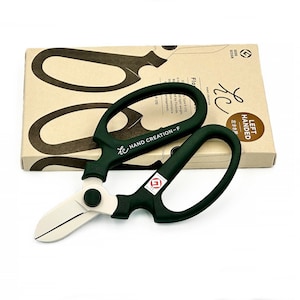 Puede incluir: Tijeras de poda verdes para zurdos con una cuchilla plateada. Las tijeras están sobre una caja marrón con el texto "LEFT HANDED" y "HAND CREATION-F" impreso en ella.