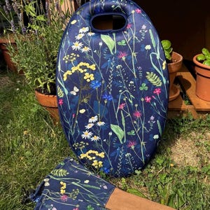 May include: An oval-shaped foam kneeling pad and a pair of gardening gloves featuring a dark blue background with a colorful botanical print of white daisies, yellow flowers, pink blossoms, and green foliage. The gloves have tan leather palms.