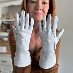 May include: A pair of white leather gloves with a brown leather cuff. The gloves have a logo on the back of the hand that says "Made in Scotland".