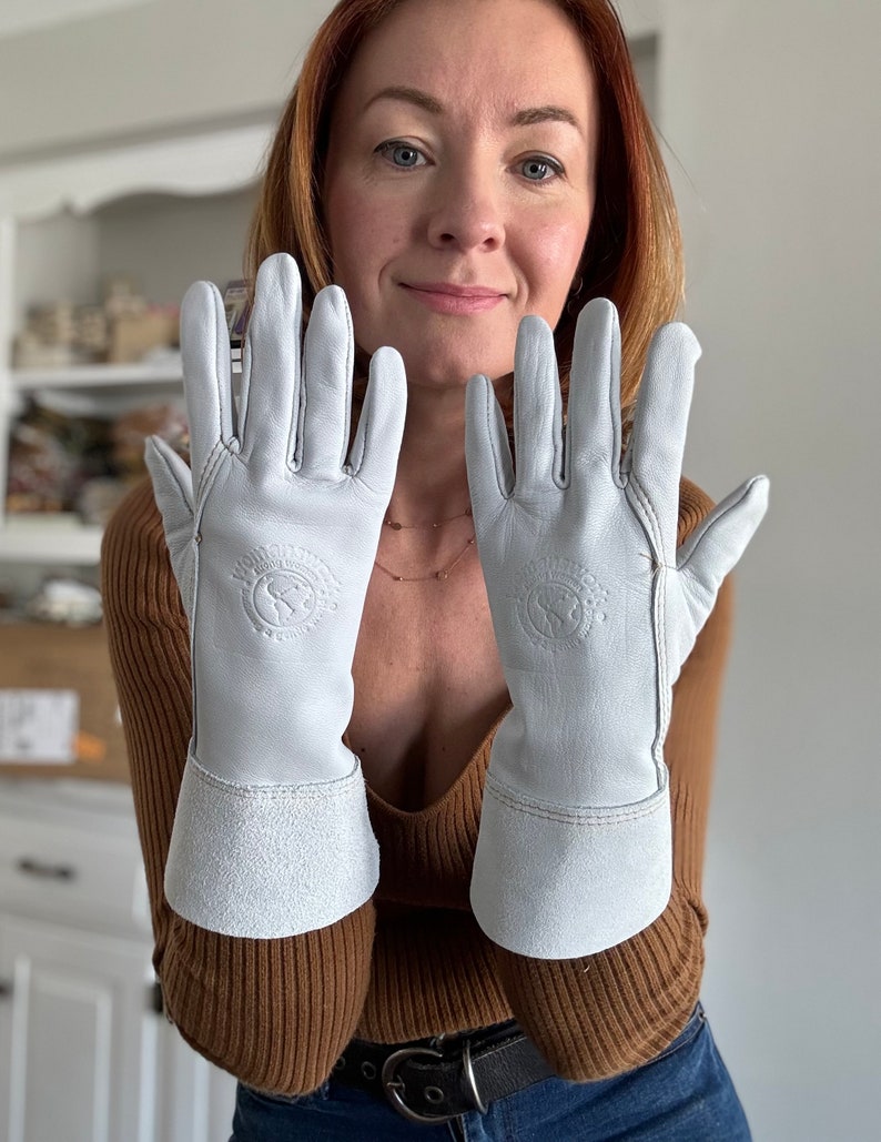 May include: A pair of white leather gloves with a brown leather cuff. The gloves have a logo on the back of the hand that says "Made in Scotland".