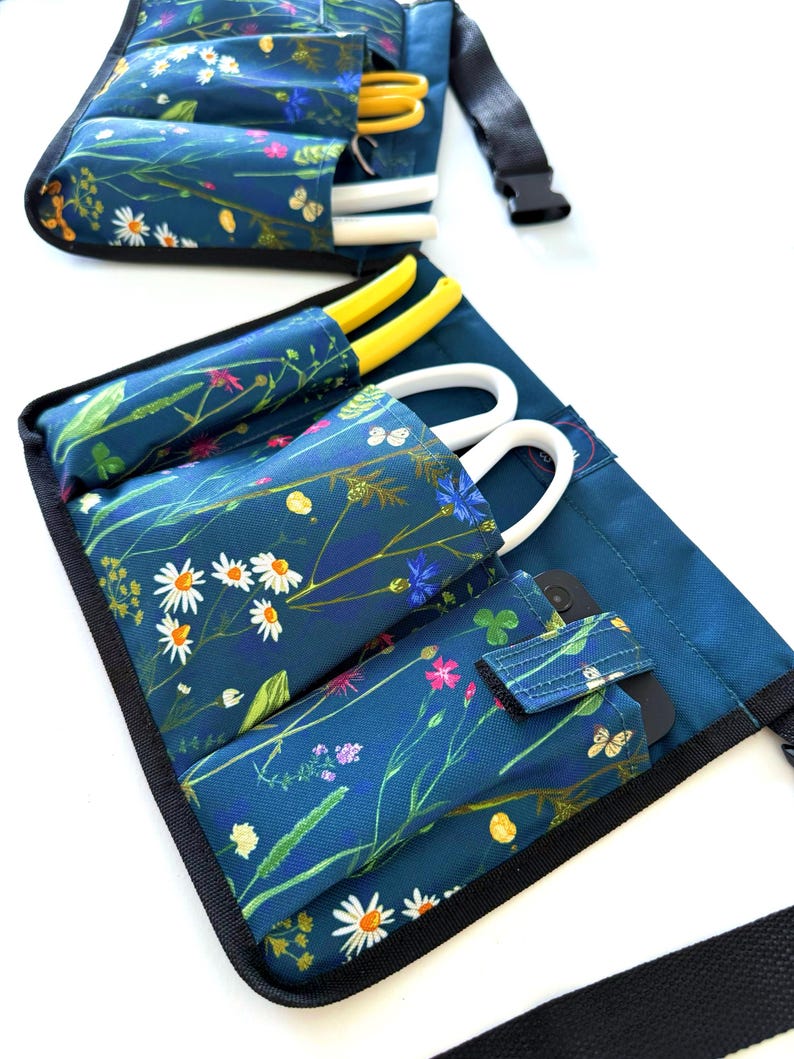 May include: A teal gardening tool belt with multiple pockets and a black adjustable strap. The belt is decorated with a floral print of white daisies, pink flowers, and green leaves.