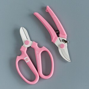 May include: Two pink gardening shears, one with a curved blade and one with a straight blade. Both shears have the text "HC HAND CREATION" printed on them.