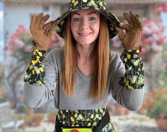 May include: A woman wearing a gray sweater and a floral print skirt with a matching hat and gloves. She is holding gardening tools in her hands.