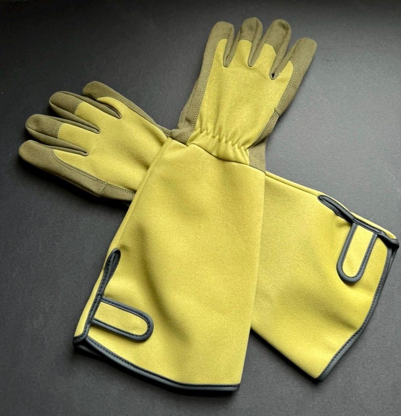 Op de afbeelding: Een paar gele tuinhandschoenen met zwarte bies. De handschoenen hebben lange mouwen die voorbij de pols reiken.