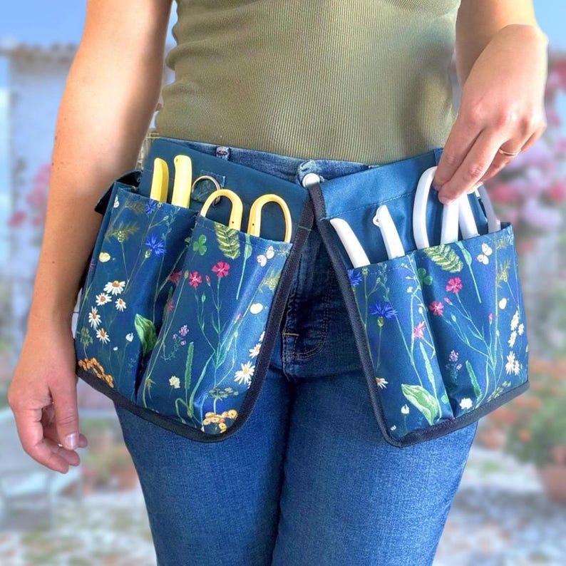 May include: A blue gardening tool belt with multiple pockets and floral print. The belt is worn around the waist and has various gardening tools in the pockets.