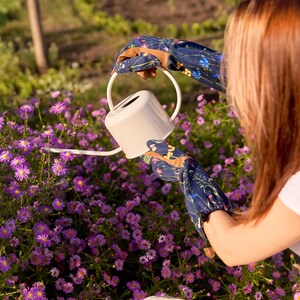 May include: A person wearing floral gardening gloves waters a bed of purple flowers with a white watering can.