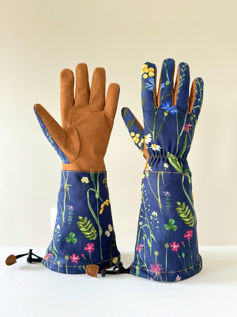 May include: A pair of gardening gloves with a floral print. The gloves are blue with a brown leather palm and have a long cuff that can be pulled up to protect the forearms. The gloves have a drawstring closure at the wrist.