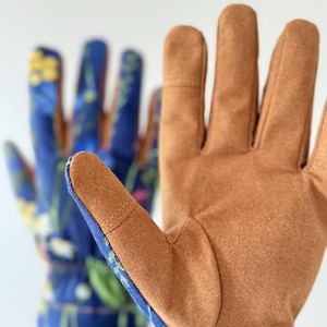 May include: A pair of gardening gloves with brown leather palms and blue fabric with a floral pattern on the back of the hand.