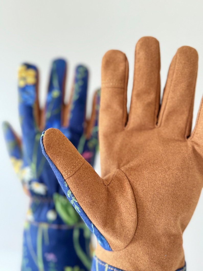 May include: A pair of gardening gloves with brown leather palms and blue fabric with a floral pattern on the back of the hand.
