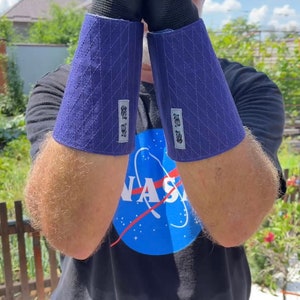 May include: A person wearing a black t-shirt with a blue NASA logo and a pair of blue and black arm guards. The arm guards have a quilted design and a white label with Japanese text.