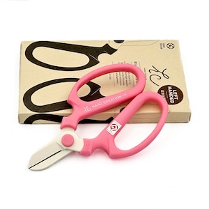 May include: Pink left-handed floral shears with a white blade. The shears are labeled "HAND CREATION-F" and "LEFT HANDED".
