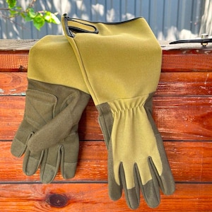 Op de afbeelding: Een paar lange, groene en bruine tuinhandschoenen met een zwarte manchet. De handschoenen zijn gemaakt van een dik, duurzaam materiaal en hebben een textuur.