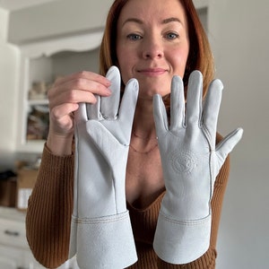 May include: A pair of white leather gloves with a cuff. The gloves have a logo on the back of the right glove.