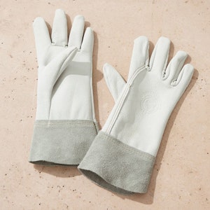 May include: A pair of white leather gardening gloves with grey suede cuffs. The gloves have a stitched seam detail and a small logo on the back of one glove.