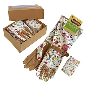 Op de afbeelding: Een tuincadeauset met een paar tuinhandschoenen met bloemenprint, een stukje tuinhoondzeep en een bruine kartonnen doos. De handschoenen hebben een bruine leren manchet en een gesp. De zeep is verpakt in wit papier met een bloemenontwerp en de tekst "Tuinhandzeep". De doos heeft een transparant plastic venster aan de bovenkant.