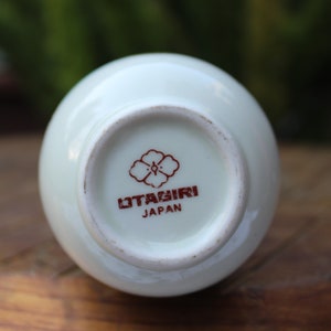 Puede incluir: Jarr&oacute;n de cer&aacute;mica blanco con un dise&ntilde;o de flor roja y blanca y el texto "Otagirl Japan" en la parte inferior.