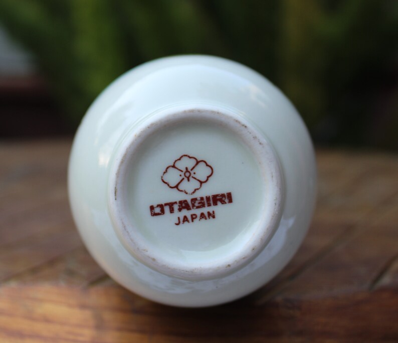 Puede incluir: Jarr&oacute;n de cer&aacute;mica blanco con un dise&ntilde;o de flor roja y blanca y el texto "Otagirl Japan" en la parte inferior.