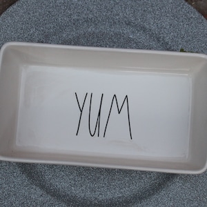 May include: White ceramic baking dish with the word "YUM" written in black on the bottom.