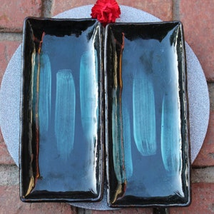 May include: Two black rectangular ceramic serving dishes with a teal glaze. The dishes have a glossy finish and are perfect for serving small snacks or appetizers.