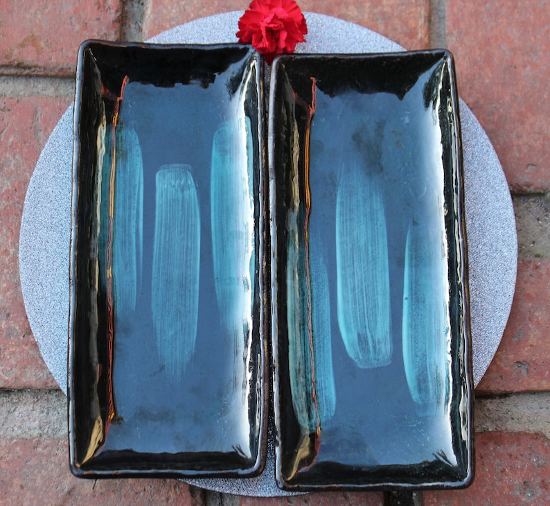 May include: Two black rectangular ceramic serving dishes with a teal glaze. The dishes have a glossy finish and are perfect for serving small snacks or appetizers.