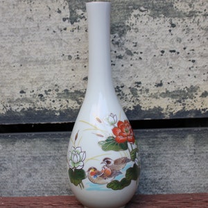 Puede incluir: Un jarr&oacute;n de cer&aacute;mica blanco con forma de l&aacute;grima y un dise&ntilde;o floral. El jarr&oacute;n presenta una flor roja, flores blancas, hojas verdes y dos p&aacute;jaros en tonos marrones, naranja y blanco.