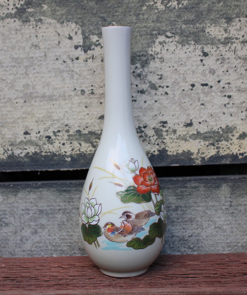 Puede incluir: Un jarr&oacute;n de cer&aacute;mica blanco con forma de l&aacute;grima y un dise&ntilde;o floral. El jarr&oacute;n presenta una flor roja, flores blancas, hojas verdes y dos p&aacute;jaros en tonos marrones, naranja y blanco.