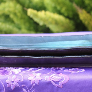 May include: Two rectangular ceramic serving plates stacked on top of each other. The top plate is a dark teal color and the bottom plate is a dark purple color. Both plates have a slightly wavy edge.