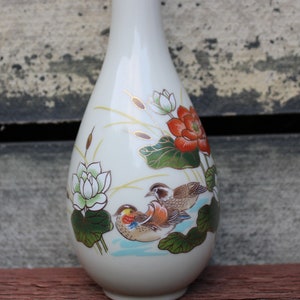 Puede incluir: Un jarr&oacute;n de cer&aacute;mica blanca con un dise&ntilde;o floral que presenta p&aacute;jaros, flores de loto y hojas. El jarr&oacute;n tiene un borde dorado y un dise&ntilde;o delicado y elegante.