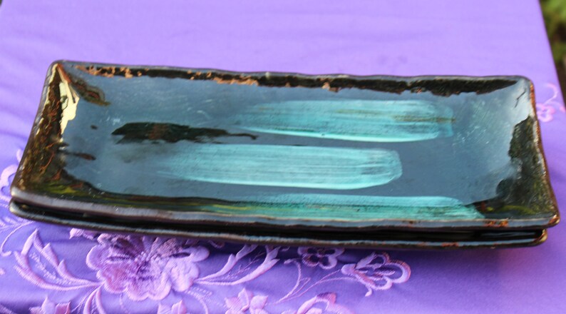 May include: A set of three black and teal rectangular ceramic serving dishes. The dishes are stacked on top of each other.