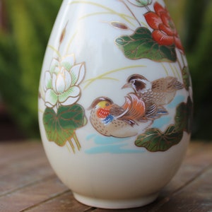 Puede incluir: Un jarr&oacute;n de cer&aacute;mica blanca con un dise&ntilde;o floral y de p&aacute;jaros. El jarr&oacute;n est&aacute; decorado con flores de loto, hojas y dos p&aacute;jaros en tonos marrones, naranjas y amarillos.