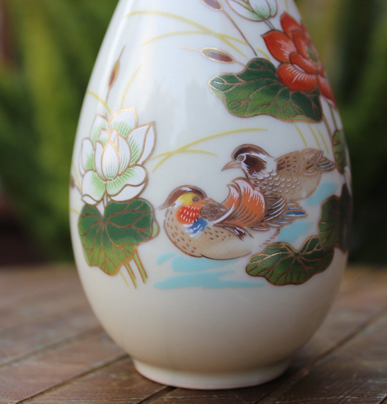 Puede incluir: Un jarr&oacute;n de cer&aacute;mica blanca con un dise&ntilde;o floral y de p&aacute;jaros. El jarr&oacute;n est&aacute; decorado con flores de loto, hojas y dos p&aacute;jaros en tonos marrones, naranjas y amarillos.